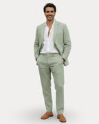 Man smiling wearing a sage green linen suit with open-collar white shirt and tan loafers, front view
