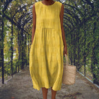 Yellow sleeveless midi dress with a gathered waist and raised dot texture, worn on a garden path.