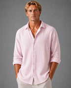 Man wearing a pink textured cotton shirt with collar open, untucked, paired with beige pants, front view