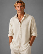 Man wearing an apricot/cream textured cotton shirt, buttoned front, sleeves rolled to forearm
