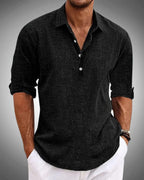Man wearing a black textured long-sleeve popover shirt with open collar and button placket, sleeves rolled to the forearm
