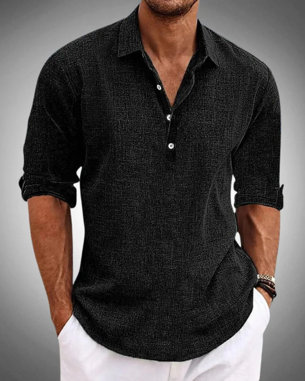 Man wearing a black textured long-sleeve popover shirt with open collar and button placket, sleeves rolled to the forearm