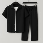 Black ribbed short-sleeve camp shirt and tapered drawstring trousers displayed on hangers against a grey backdrop