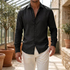 Front view of a model wearing a charcoal black long-sleeve shirt with pointed collar, fully buttoned, with cream trousers
