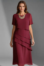 Model wearing a deep red tiered chiffon dress with short sleeves and a layered gold necklace