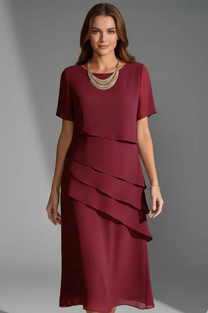 Model wearing a deep red tiered chiffon dress with short sleeves and a layered gold necklace