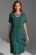Model wearing an emerald green tiered chiffon dress with short sleeves and round neckline, front view