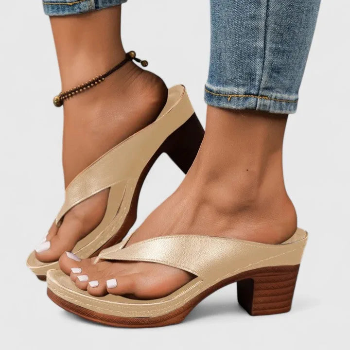 Gold-tone toe-post sandal shown side-on, worn with rolled-up jeans and a beaded anklet