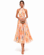 Woman in a peach watercolour floral halter neck midi dress holding a beaded clutch, front view