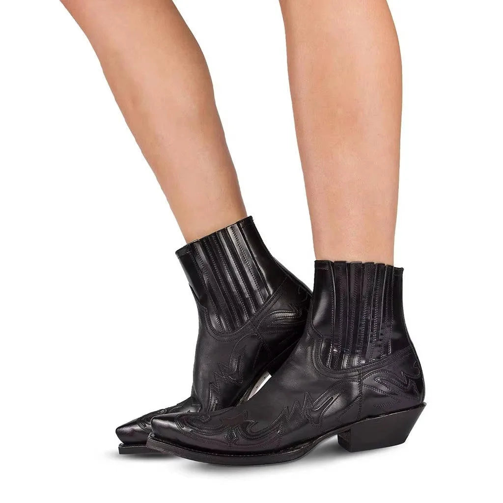 Side view of black leather western ankle boots with pointed toe and flame-stitch embroidery, worn on model's legs