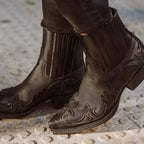 Close-up of model walking in black leather western ankle boots with jeans, showing stitched flame detailing