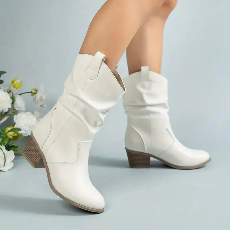 White slouch western boots with pointed toe and stacked heel styled against a soft blue backdrop