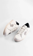 Top-down view of a paired set of white leather sneakers showing cream laces and distressed sole edges.