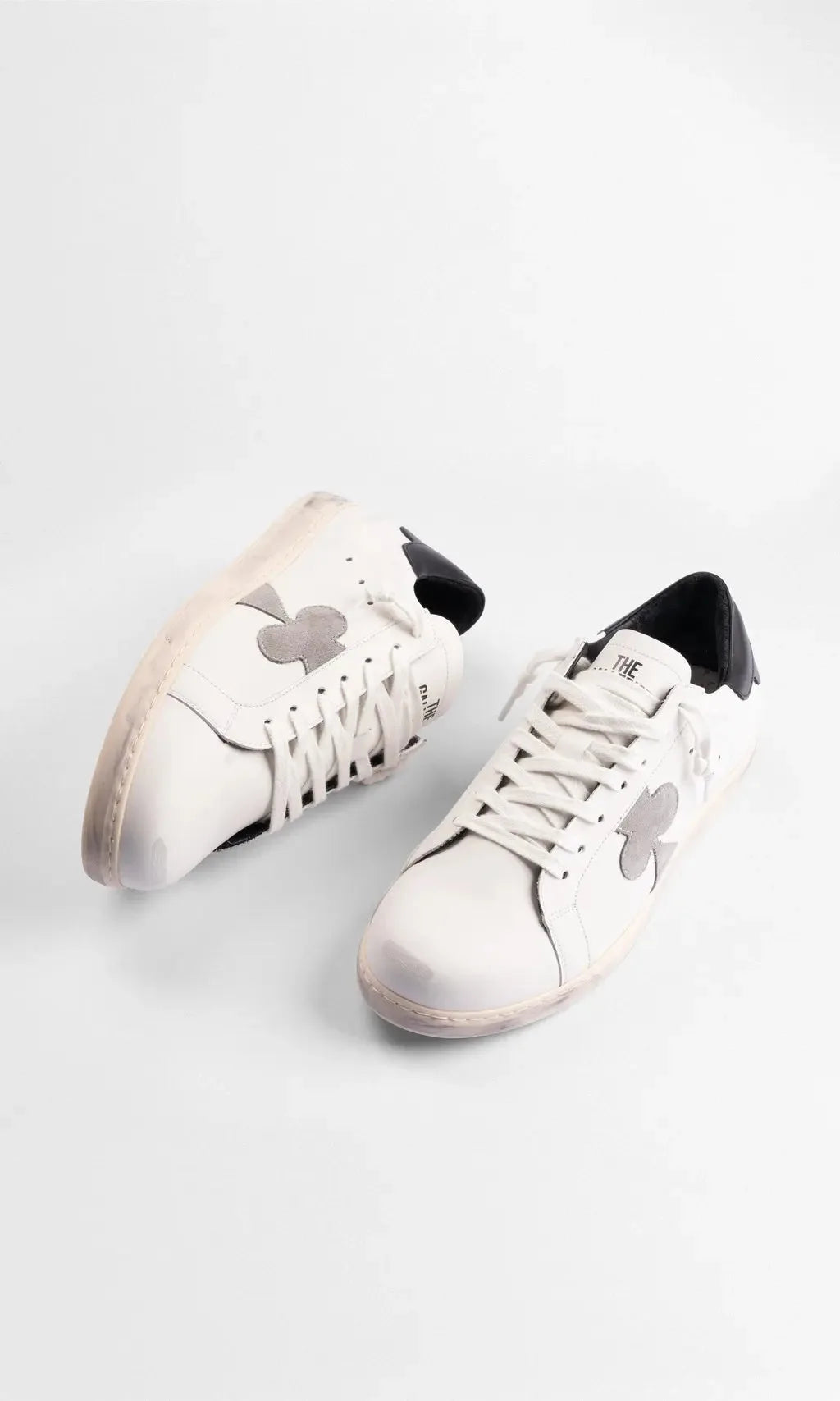 Top-down view of a paired set of white leather sneakers showing cream laces and distressed sole edges.