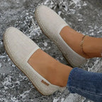 Close-up of beige woven espadrille flats worn on bare feet, showing braided jute trim and gold anklet