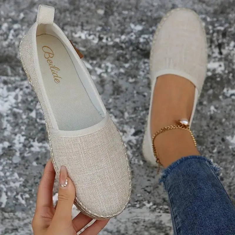 Inside view of a beige espadrille flat held in hand, revealing soft textile lining and brand label