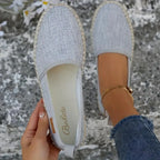 Grey textured espadrille flat held up beside a matching shoe worn on foot, showing jute sole edge