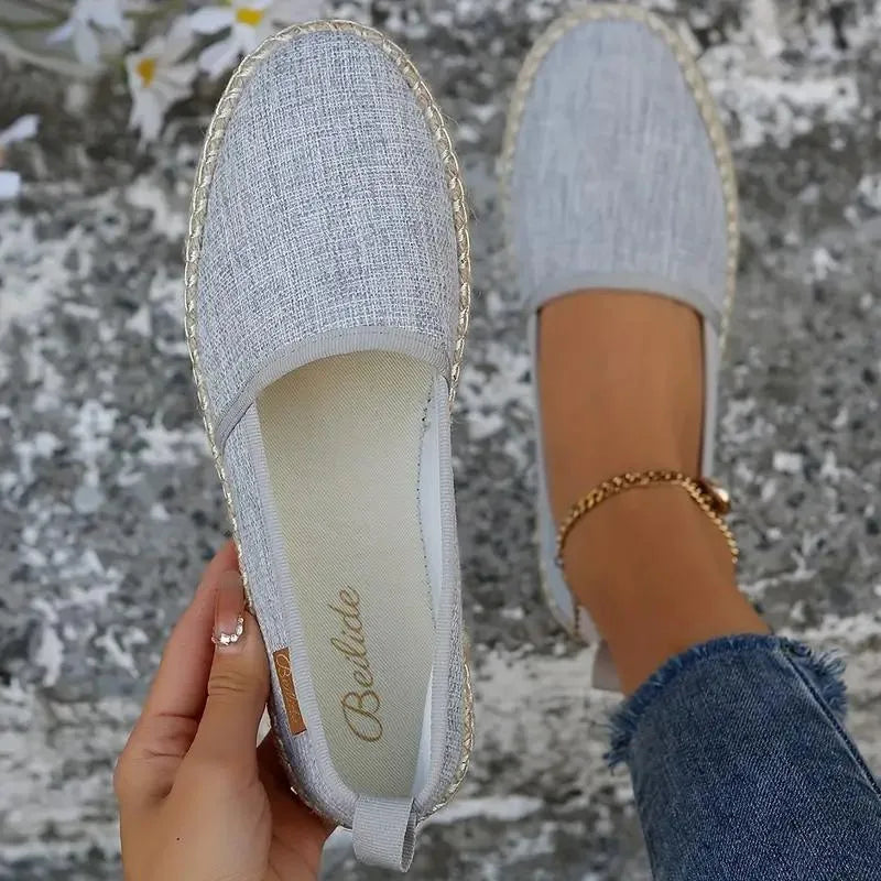 Grey textured espadrille flat held up beside a matching shoe worn on foot, showing jute sole edge