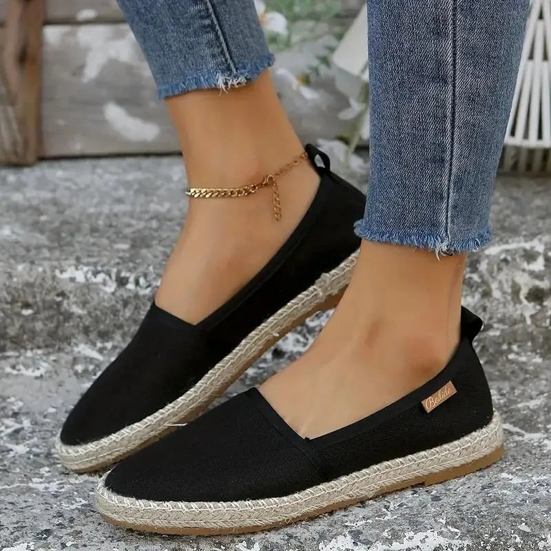 Black canvas espadrille flats worn on both feet with cropped jeans, showing round toe and jute sole