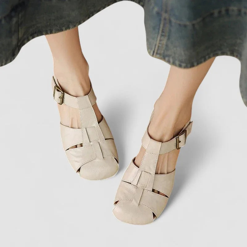 Overhead view of beige leather fisherman sandals with buckle straps worn on both feet with denim skirt