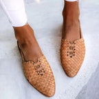 Close-up front view of tan woven leather flats with pointed toe and lace-up detail, worn barefoot