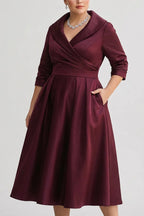 Front view of the wrap midi dress in rich burgundy satin with hand resting in the side pocket, showing the fit-and-flare silhouette.
