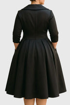 Back view of the midi dress in black satin, showing the fitted bodice seaming, waistband and the deep box-pleated skirt.