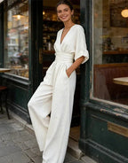 Woman in a white wrap-front wide-leg jumpsuit with puff sleeves, leaning in a doorway outside a café