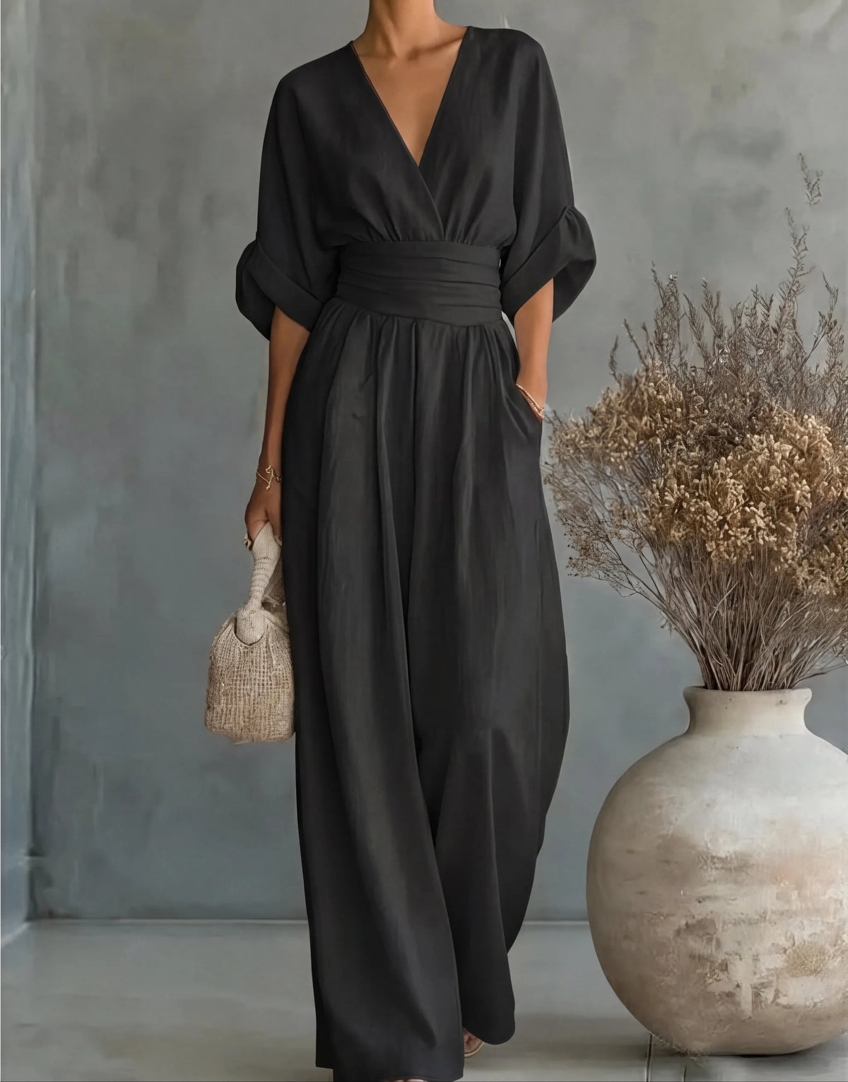 Detail shot of the ruched waist tie on the cream wrap jumpsuit against a neutral wall