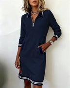 Front view of navy polo dress with zip collar, ribbed cuffs and striped hem detail, hand in pocket