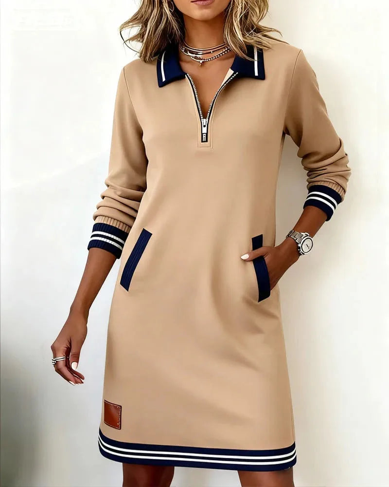 Beige polo dress with navy collar and cuffs, striped hem, worn with hand resting in side pocket