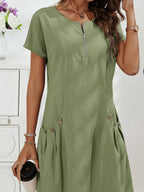 Sage green midi dress close-up highlighting the decorative button pockets set into the gently flared skirt